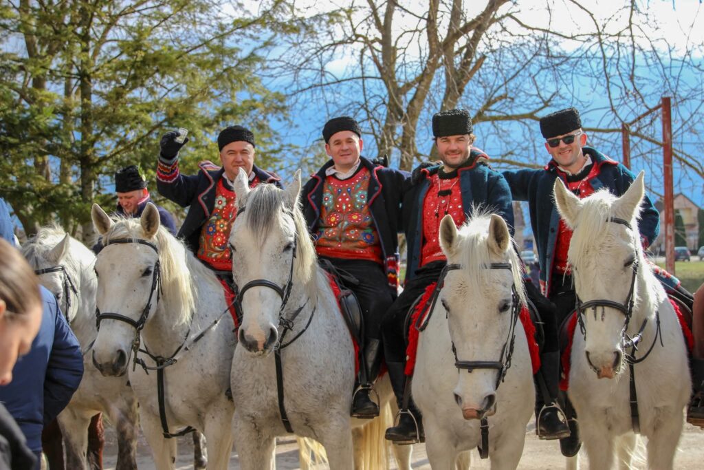 Četiri jahača u tradicionalnim vezenim prslucima i šubarama na bijelim konjima nazdravljaju na pokladnom jahanju u Cerni