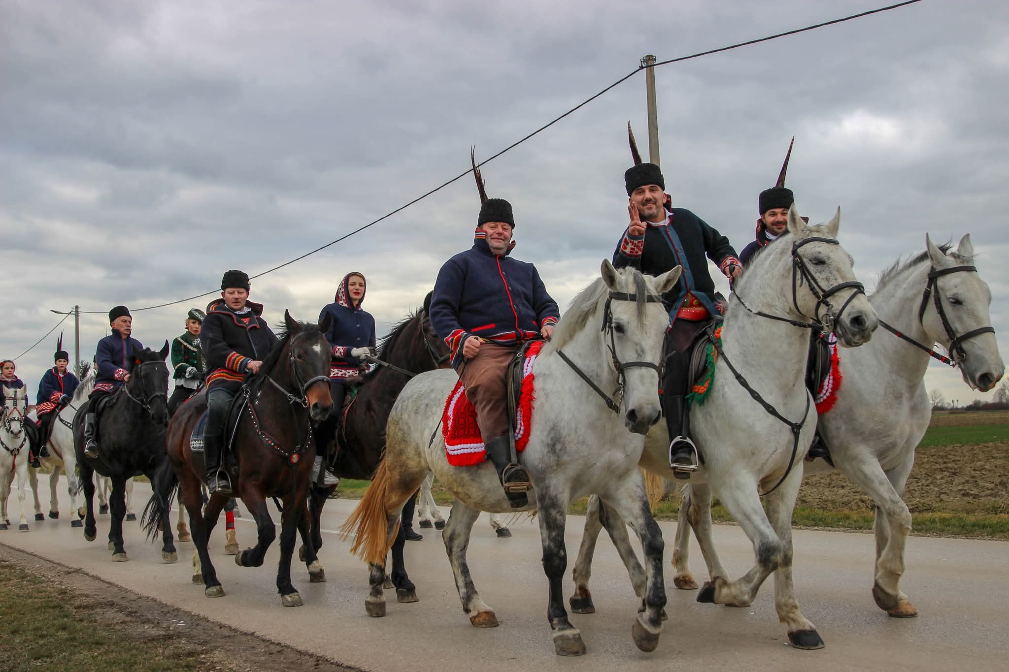 Povorka jahača u tradicionalnim nošnjama i šubarama s perjem na bijelim i smeđim konjima na seoskoj cesti